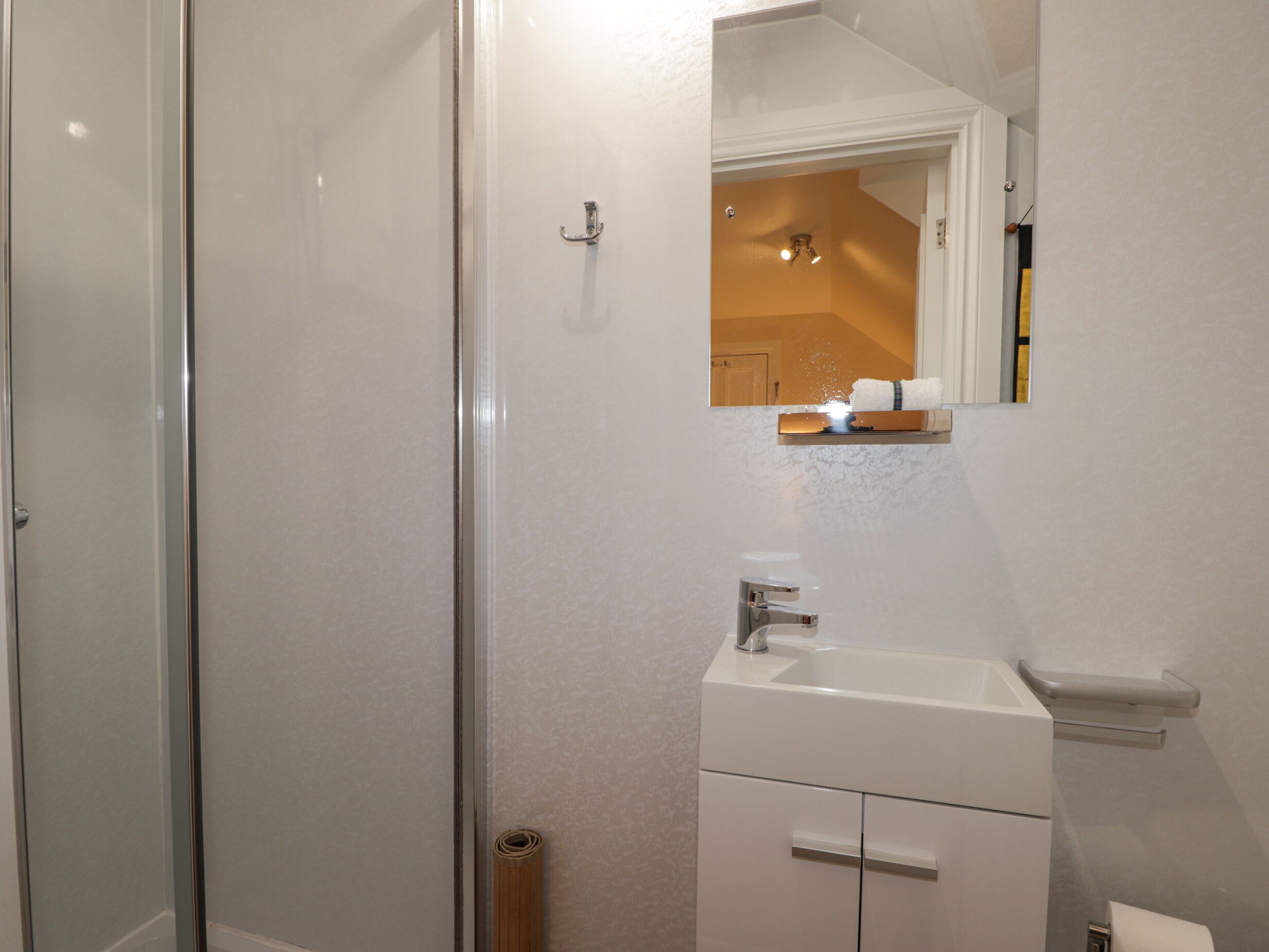 Un baño moderno con cabina de ducha de vidrio, un lavamanos blanco con un espejo encima y un perchero para toallas.