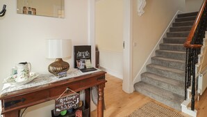 Ein Holztisch mit einer Lampe, einem Willkommensschild und einem gerahmten Bild. Eine Holztreppe mit Geländer führt zu einer Zwischenebene.