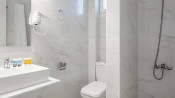 Een moderne badkamer met een marmeren vloer, een witte wastafel met toiletartikelen, een toilet en een douchehoek.