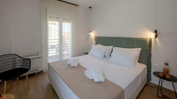 Quarto de hotel com uma cama, uma cadeira, uma mesa com garrafa e copos, e um ventilador de teto.