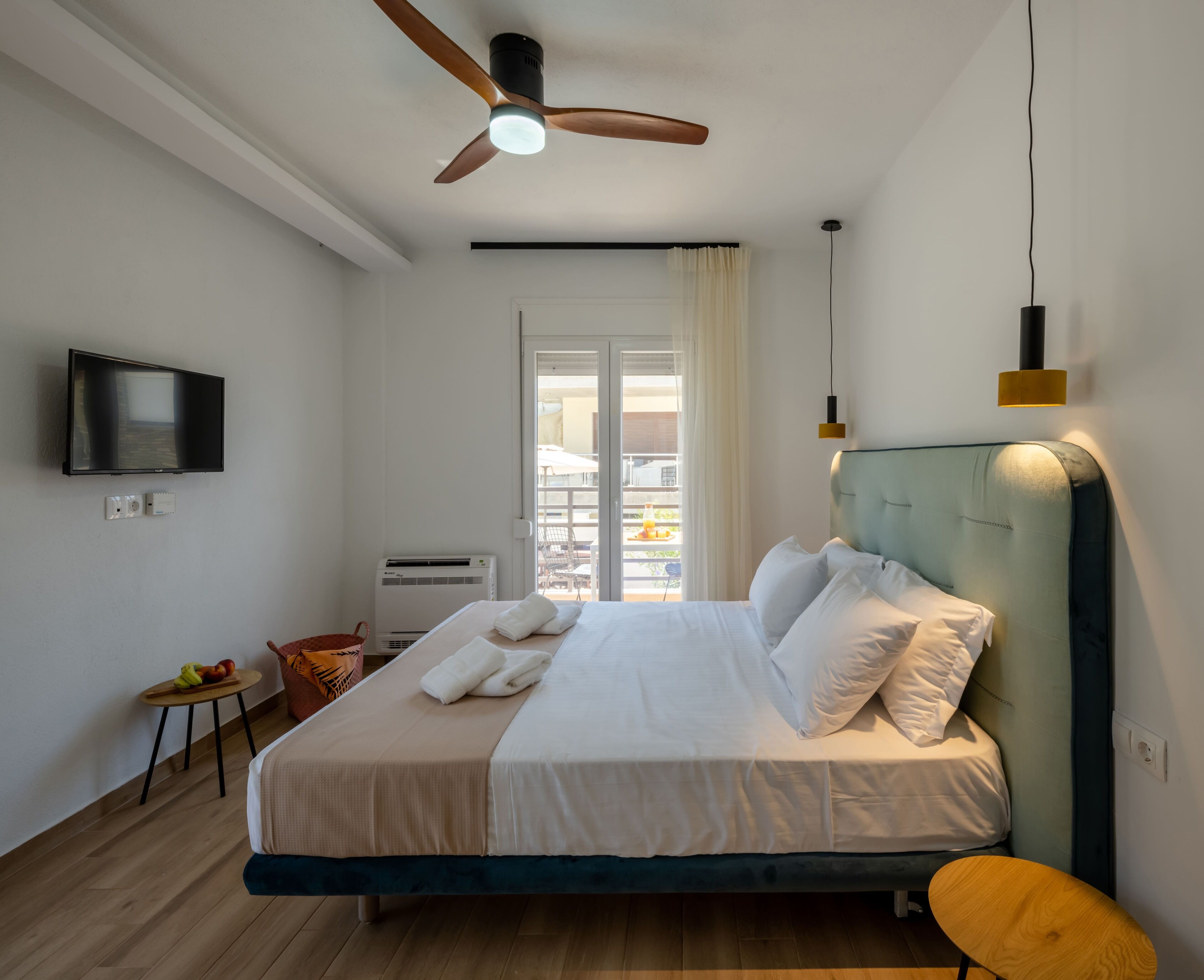Une chambre d’hôtel moderne équipée d’un lit, d’un ventilateur de plafond, d’une télévision et d’une fenêtre avec des rideaux.