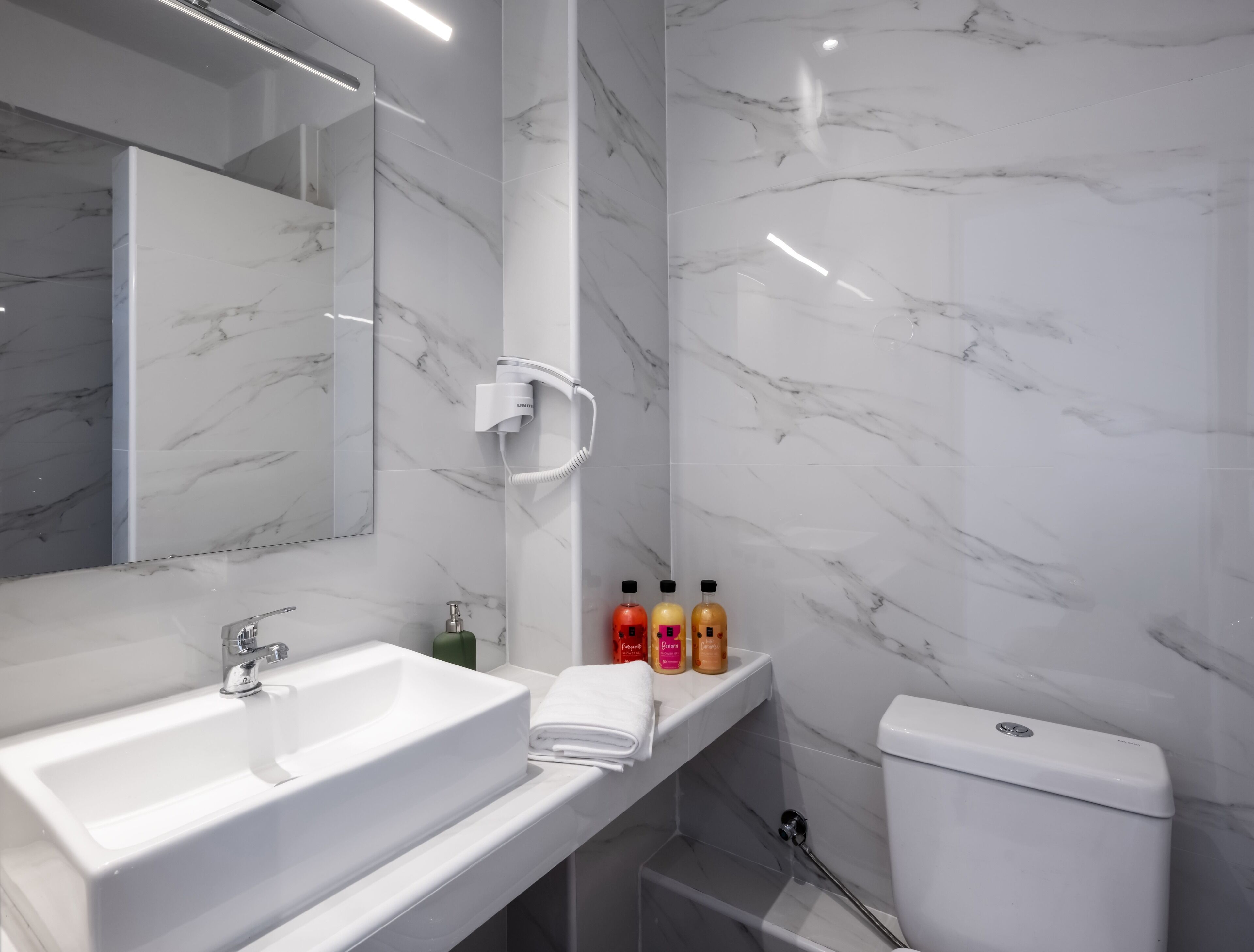 A modern bathroom with a white sink, a mirror, a toilet, and a shelf with toiletries.