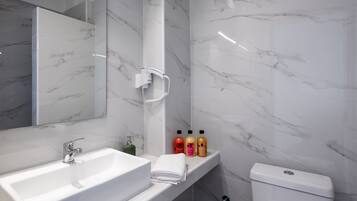A modern bathroom with a white sink, a mirror, a toilet, and a shelf with toiletries.