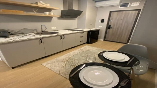A modern kitchen with a built-in oven, a sink, and a dining area with a table set for two. - EM04- Studio premium - pat matrimonial (Târgu Jiu)