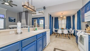 Een moderne keuken met blauwe kastjes, een wit aanrecht en een eethoek met een kroonluchter.