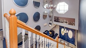 Een trap met een houten leuning en witte spijlen, leidend naar een woonruimte met een blauwe bank en een kroonluchter.