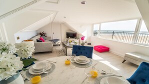 Un coin repas avec une table dressée pour deux personnes, un canapé et un balcon offrant une vue sur la plage.