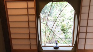 Una habitación con suelo de estera de tatami, un separador shoji y una ventana con vistas a follaje.