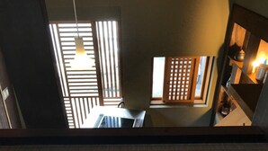 Vista desde una ventana con una puerta de madera celosíaca, una lámpara colgante y una estantería con utensilios de cocina.