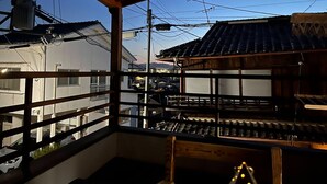 Un bâtiment japonais traditionnel, avec un toit recouvert de tuiles et des poutres en bois, vu depuis un balcon doté d’une rambarde en métal.