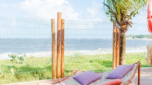 Eine Hängestuhl mit Kissen auf einer Holzterrasse mit Blick auf einen Strand.