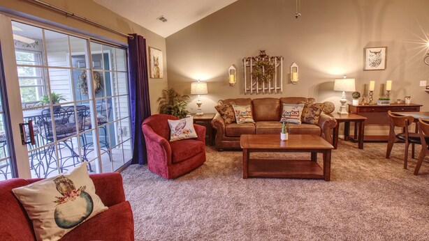 A living room with a red armchair, a brown sofa, a wooden coffee table, and a dining area with a table and chairs.