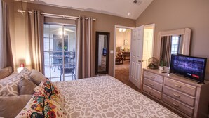 A bedroom with a large bed, a dresser, a television, and a sliding glass door leading to a balcony.