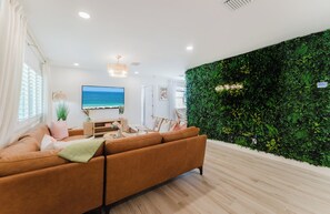 Ein modernes Wohnzimmer mit einem großen braunen Sofa, einem Flachbildfernseher, einer grünen Wand mit einer Pflanzenwand und einem Holzboden.
