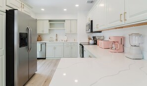 A modern kitchen with white cabinetry, stainless steel appliances, and a marble countertop.