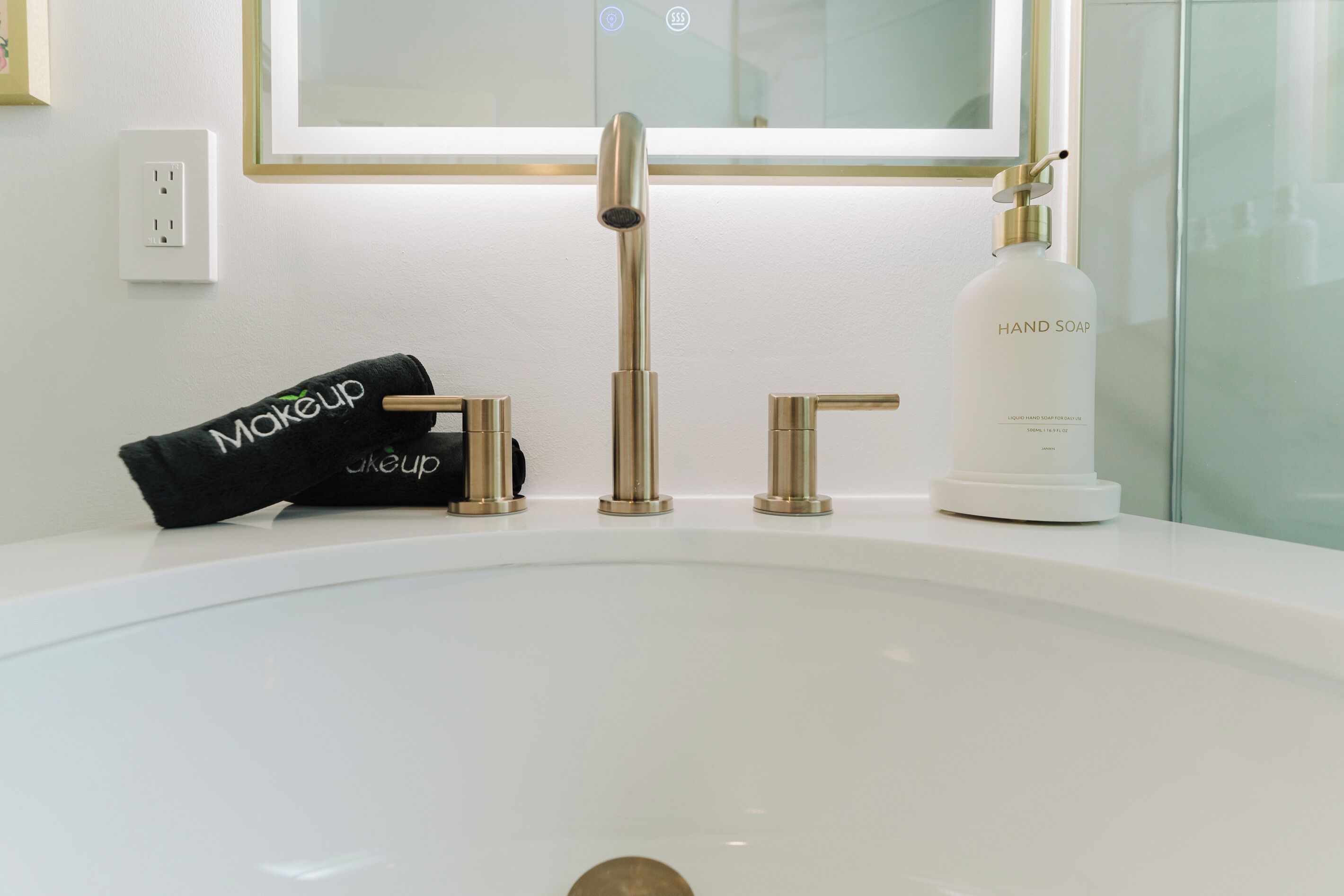 A bathroom sink with a modern faucet, a bottle of hand soap, and a black towel with the word 'makeup' on it.