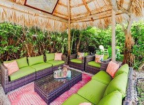 An outdoor seating area with wicker furniture and green cushions, surrounded by lush greenery.