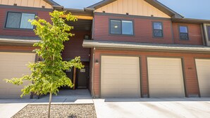 A two-story residential building with a garage, a small tree in front, and a clear sky. - Brand New Townhome - 10 Minutes from Downtown (Bozeman)