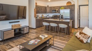 A modern kitchen with a central island, bar stools, and a flat-screen TV. - Brand New Townhome - 10 Minutes from Downtown (Bozeman)