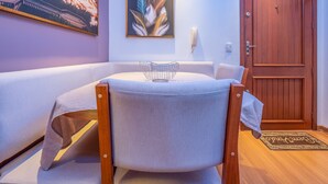 A room with a round table, a cushioned bench, a wooden door, and a wall-mounted telephone. - Apartment in Gramado city center, 100m from Rua Coberta (Gramado)