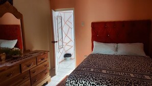 A bedroom with a red upholstered headboard, a bed with a leopard print bedspread, a wooden dresser, and a mirror.