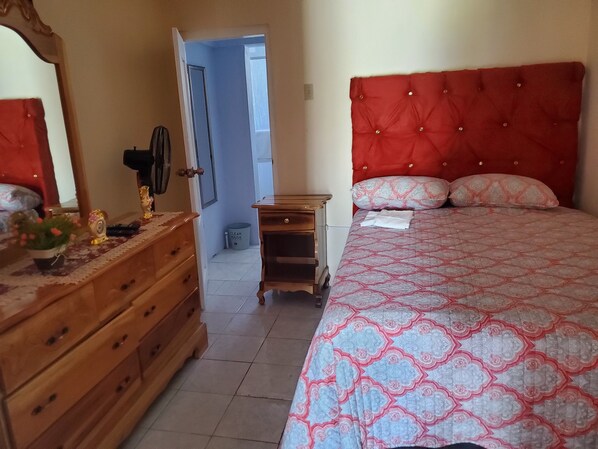 Une chambre à coucher avec une tête de lit rembourrée de tissu rouge, une commode en bois, une table de chevet et une couvre-lit à motifs.