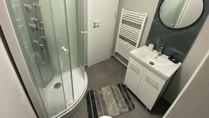 Casa de banho com chuveiro em cabine de vidro, pia branca com espelho e porta-toalhas.