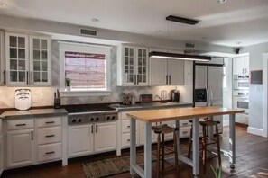 Uma cozinha moderna com armários brancos, uma ilha central com banquetas, forno embutido e geladeira.