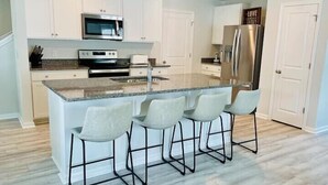 Una cocina moderna con armarios blancos, un refrigerador de acero inoxidable, un microondas y una isla grande con taburetes de bar.