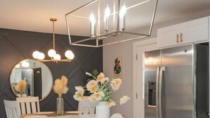 A modern kitchen with a white island, bar stools, a round mirror, and a stainless steel refrigerator.