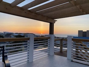 A balcony with a view of the sunset over the ocean, featuring a wooden pergola and metal railings. - Up on the Roof - Ocean Views - Arcade - Air Hockey - iRacing - Glow Golf! (Carolina Beach)