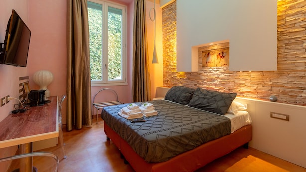 Ein Schlafzimmer mit Bett, Schreibtisch, Stuhl, Fernseher und einem Fenster mit Vorhängen.