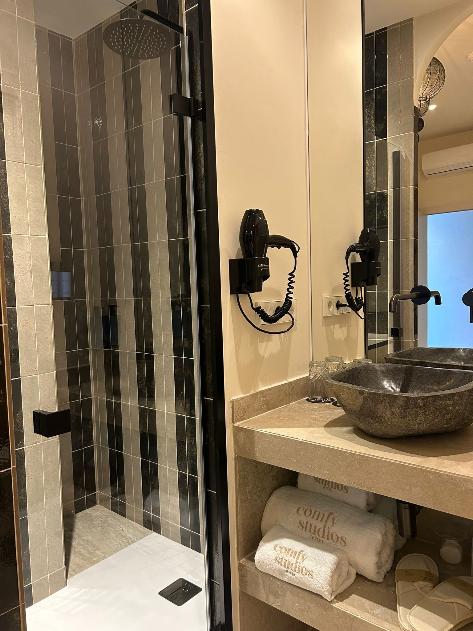 Un baño con ducha envuelta en vidrio, un lavamanos de piedra y toallas con la marca 'comfy studios'.