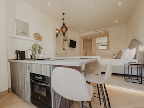 A modern kitchen with a central island, bar stools, a built-in oven, and a hanging pendant light.