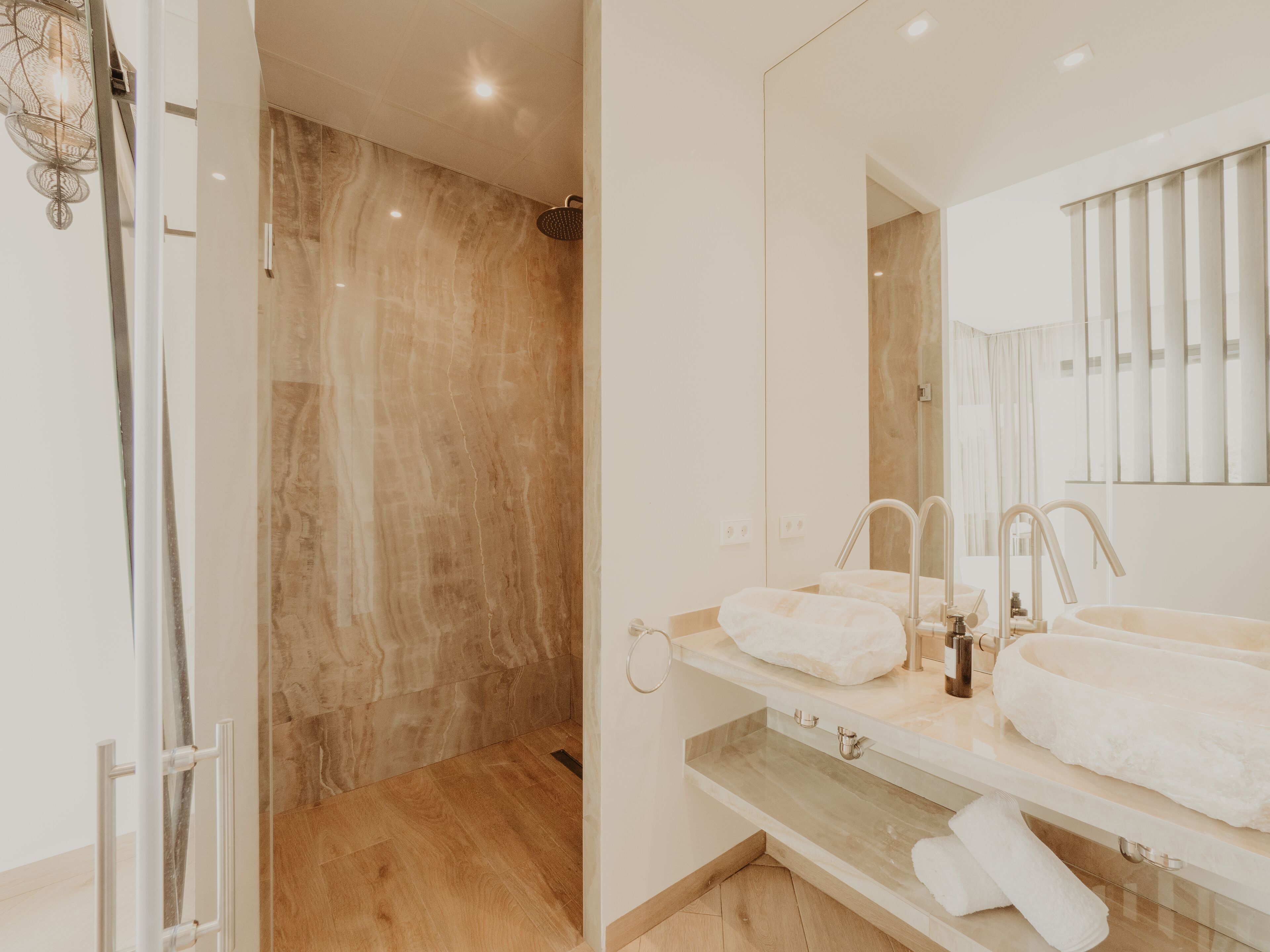 Un baño moderno con ducha acristalada, un espejo grande y dos lavamanos.