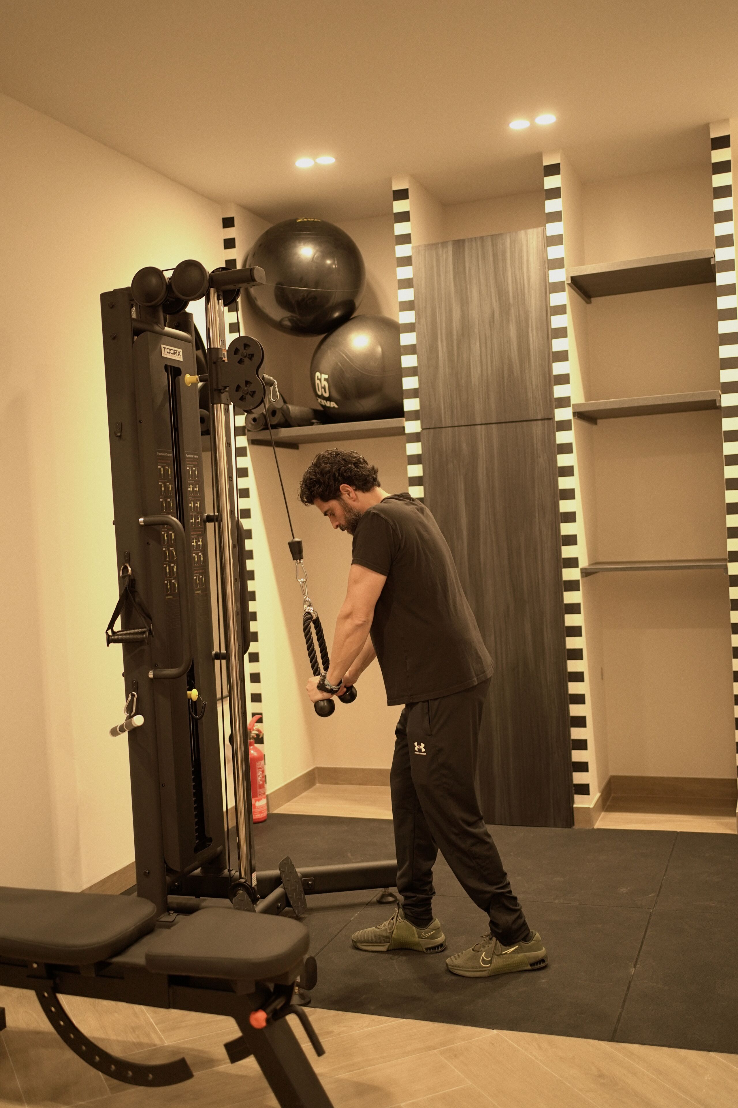 Un gimnasio con equipo de ejercicio, una banca y una pelota medicinal sujeta a la pared.