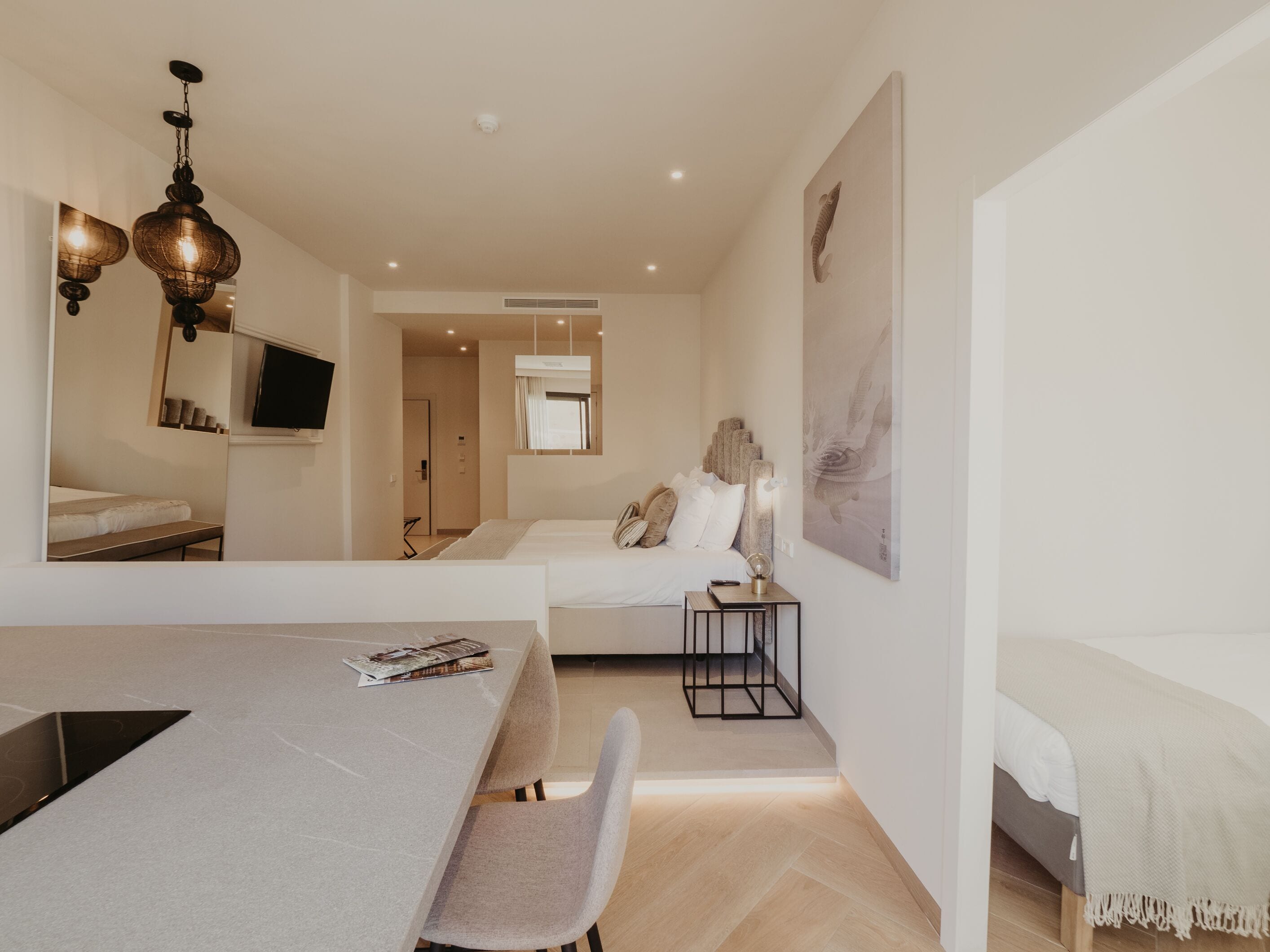 Habitación de hotel moderna con comedor, un espejo grande, cama y televisor montado en la pared.
