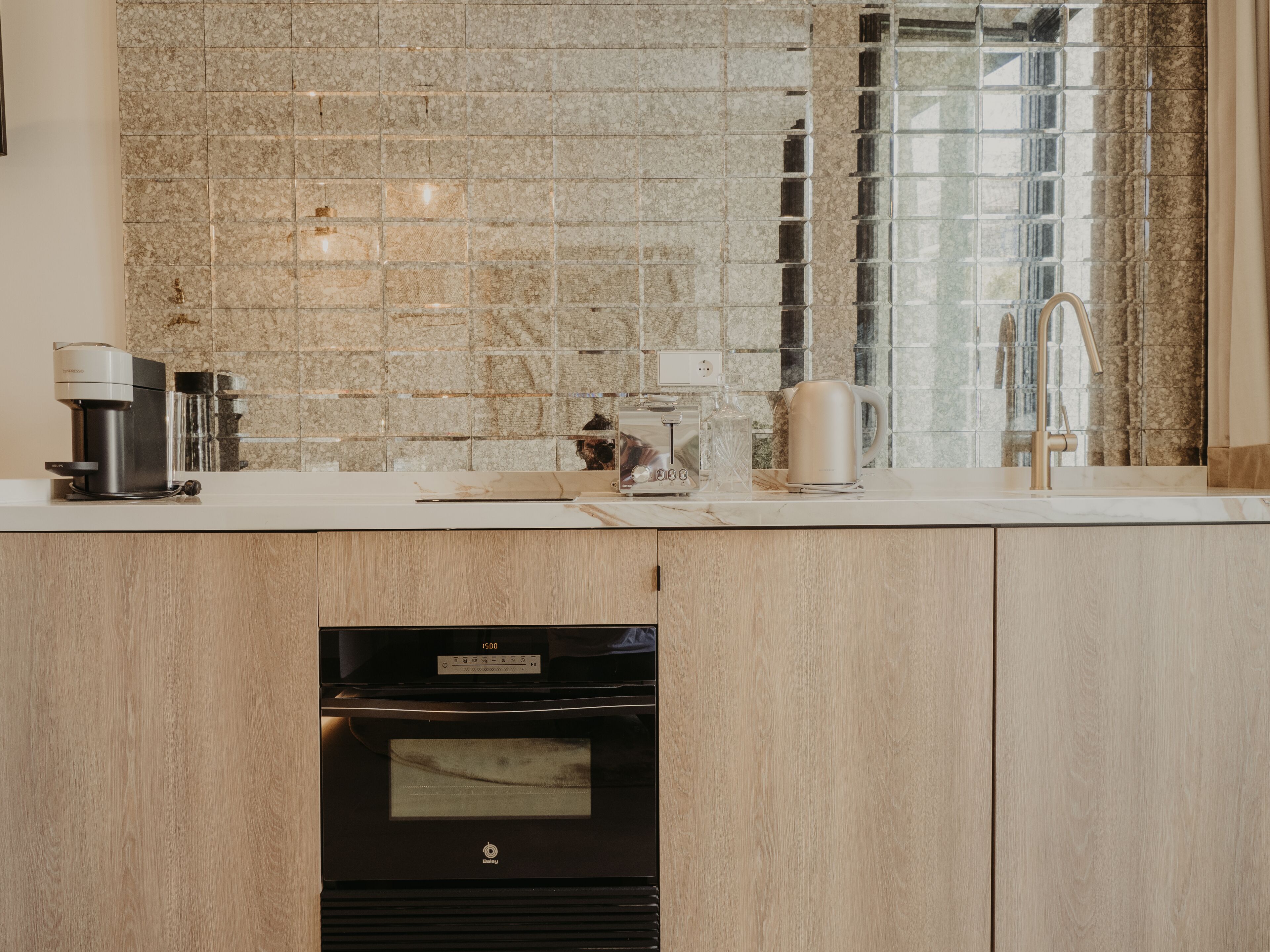 A modern kitchen with a built-in oven, a coffee maker, and a kettle on the countertop.