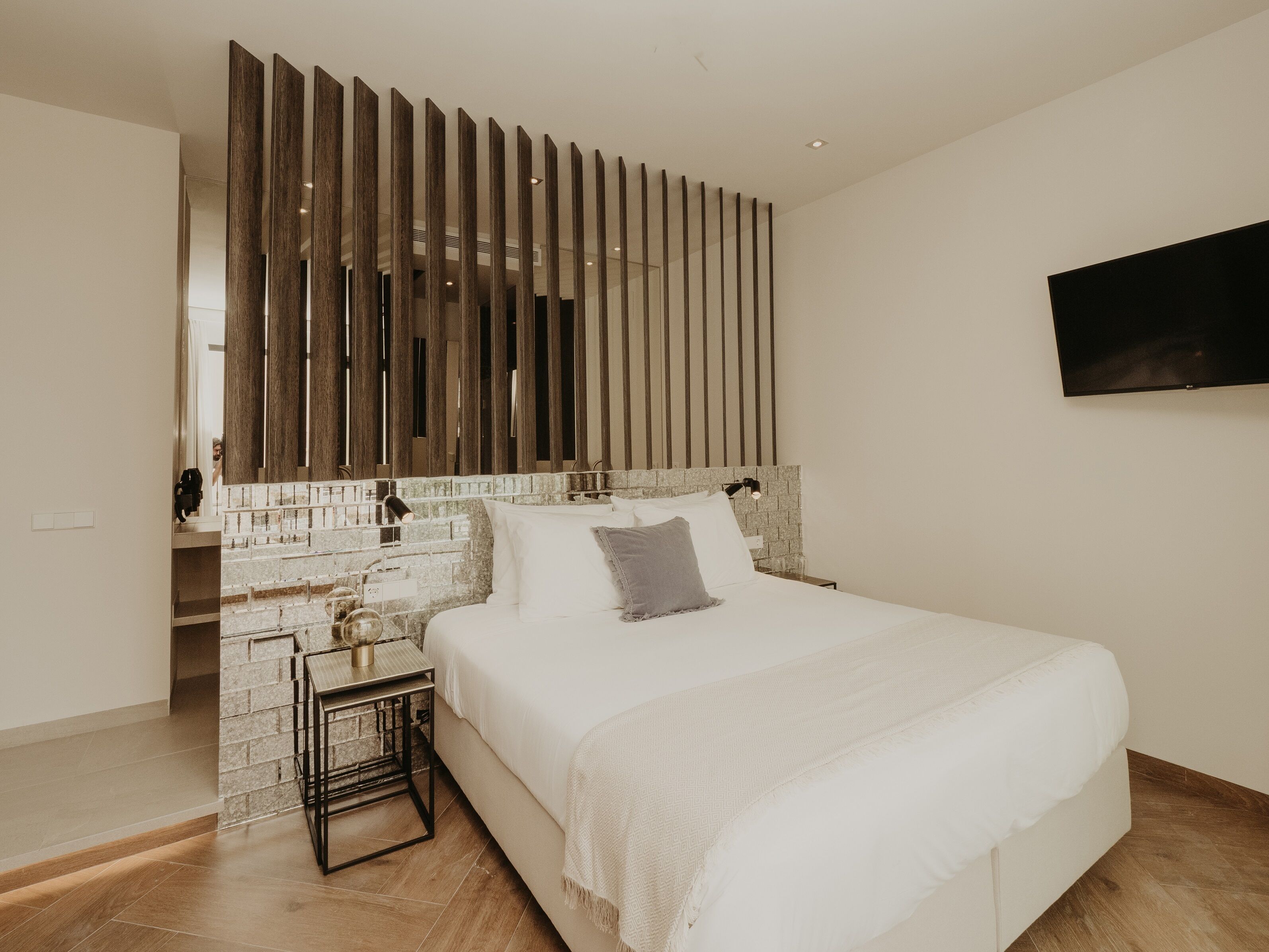 A modern bedroom with a large bed, a stone accent wall, a wooden slat partition, and a mounted TV.