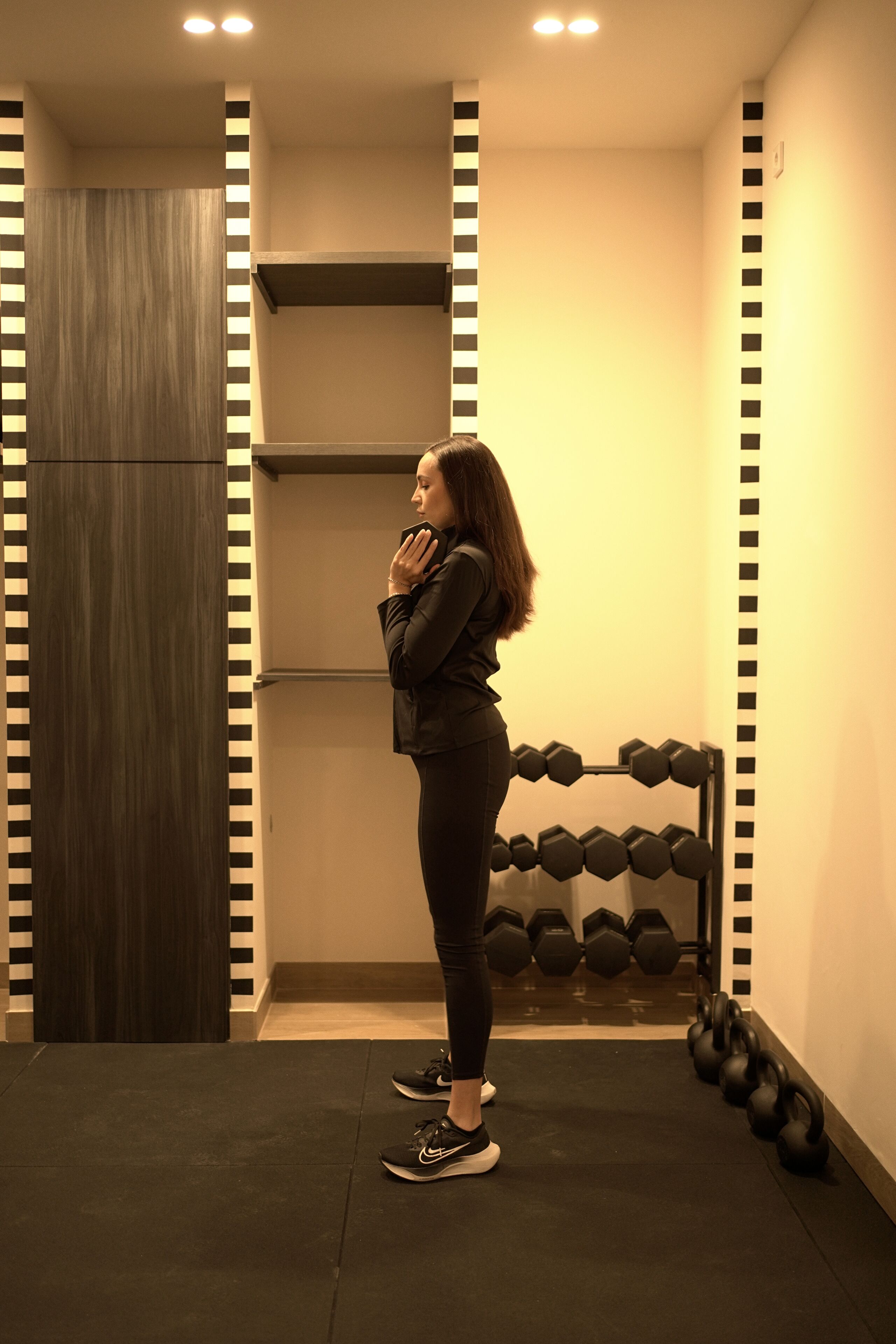A person standing in a gym with a rack of dumbbells and a wooden door.