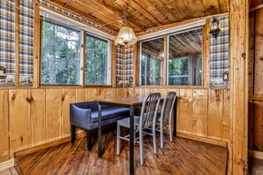 Enjoy a warm atmosphere in this inviting room with a wooden dining table, comfortable seating, and large windows overlooking the surrounding greenery.