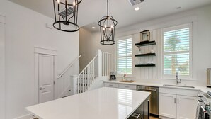 Una cocina moderna con armarios blancos, una isla grande, electrodomésticos de acero inoxidable y una escalera que sube a un altillo.