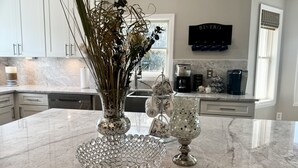Et køkken med marmorfliser, en vase med tørrede planter, en dekorativ glas skål og en kaffemaskine.
