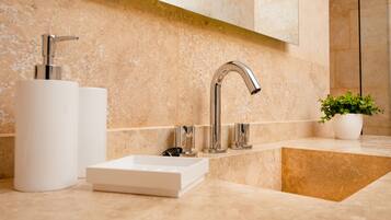 A modern bathroom with a marble countertop, a white sink, a chrome faucet, and a potted plant.