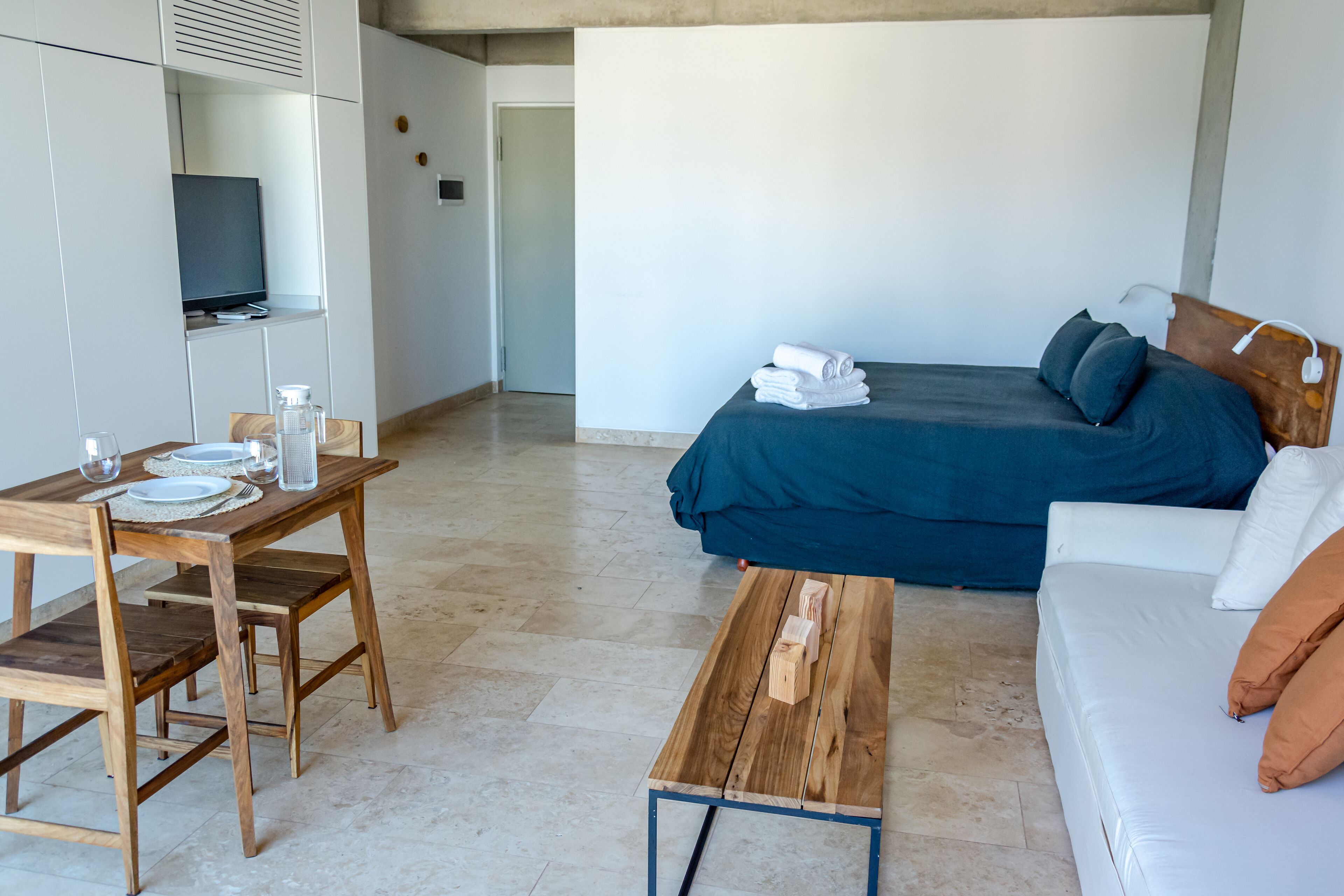 A compact hotel room with a bed, a sofa, a wooden table, and a television.