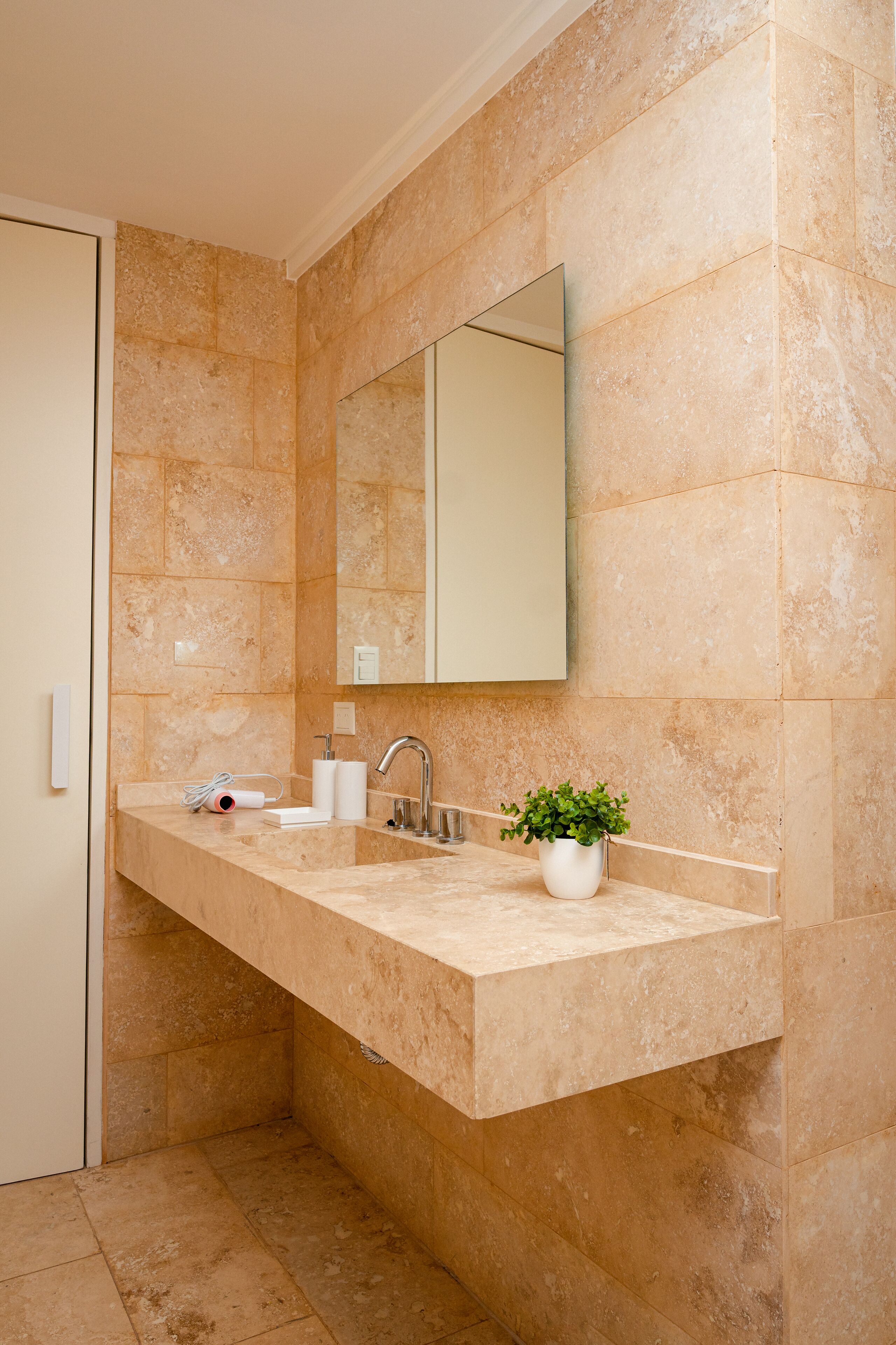 Un baño moderno con encimera de mármol color beige, un lavabo, un espejo y una planta en maceta.