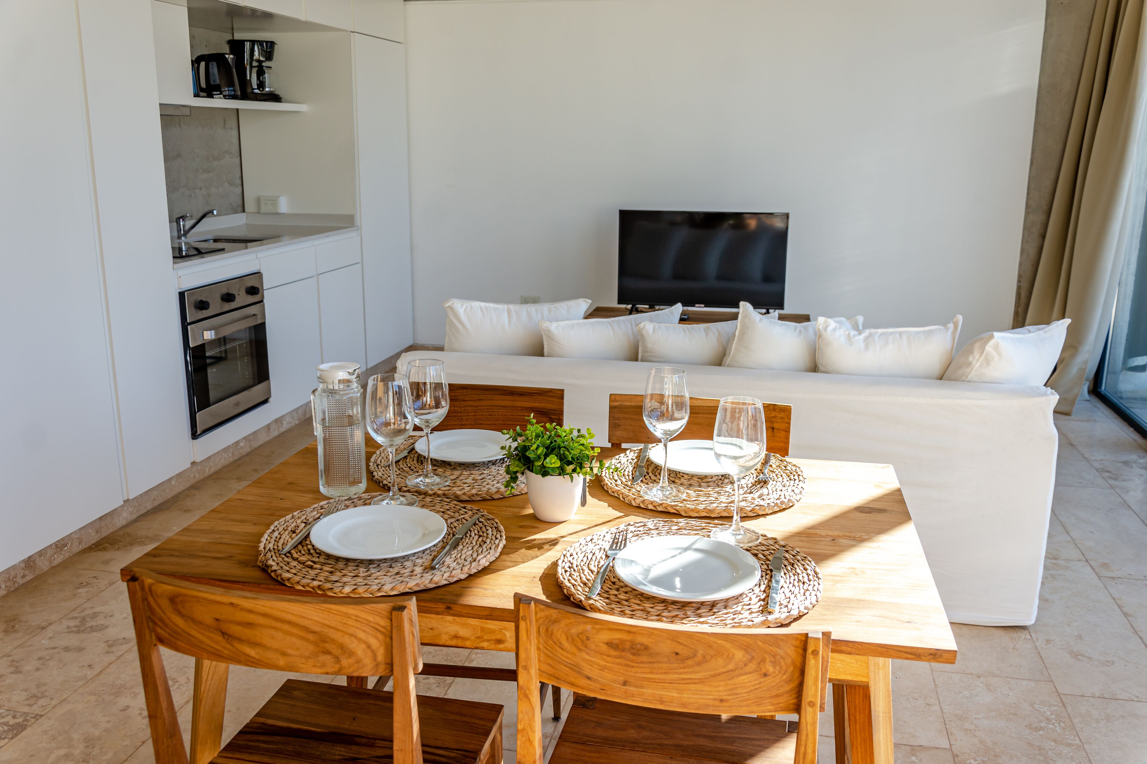 Una cocina moderna con horno empotrado y comedor con mesa de madera para cuatro.