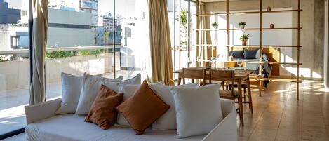 A modern living room with a white sofa, a wooden coffee table, and a view of the city through large windows.