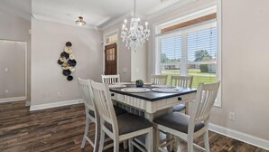 Un coin repas avec une table rectangulaire, des chaises blanches et un lustre.