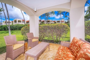 A covered outdoor seating area with wicker furniture and a view of a resort building.
